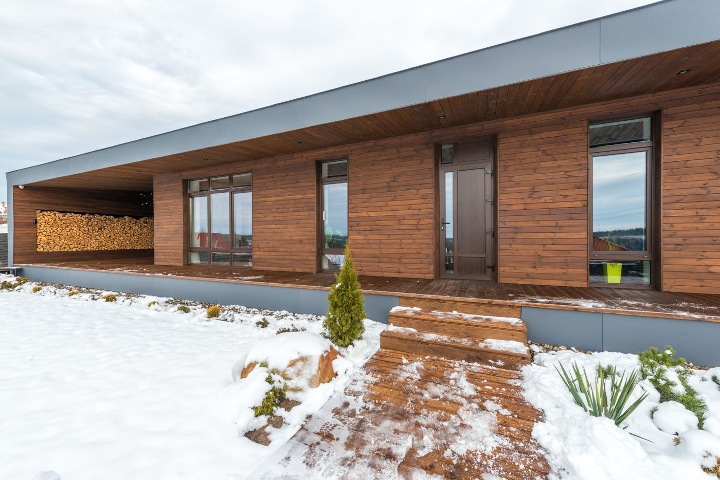 Maison contemporaine en bois avec réserve de bois de chauffage sous une lumière d'hiver